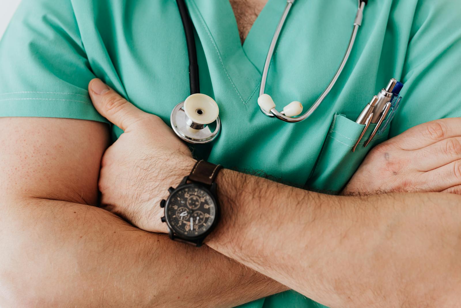 Close-up of a healthcare professional with arms crossed wearing medical scrubs and stethoscope.